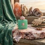 عطر آمواژ لینیج روی سنگ مرمر با پس‌زمینه ساحل، فسیل، دستکش و وسایل قدیمی دریانوردی