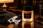 ادکلن اورجینال لالیک آمبر نویر Lalique Ombre Noire روی میز کار چوبی در کنار کت و شلوار رسمی مردانه