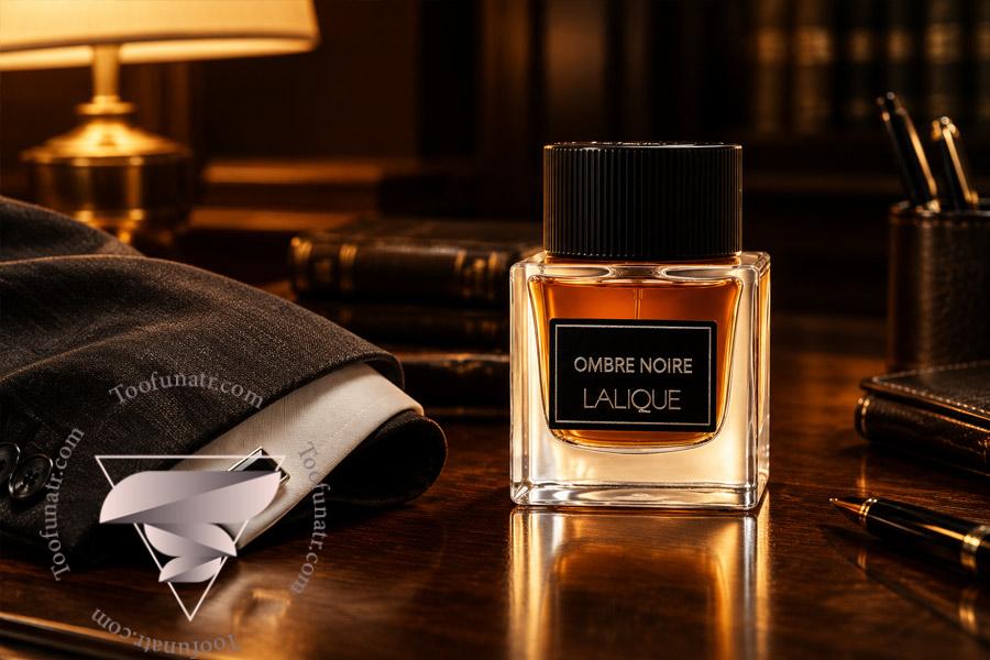 ادکلن اورجینال لالیک آمبر نویر Lalique Ombre Noire روی میز کار چوبی در کنار کت و شلوار رسمی مردانه