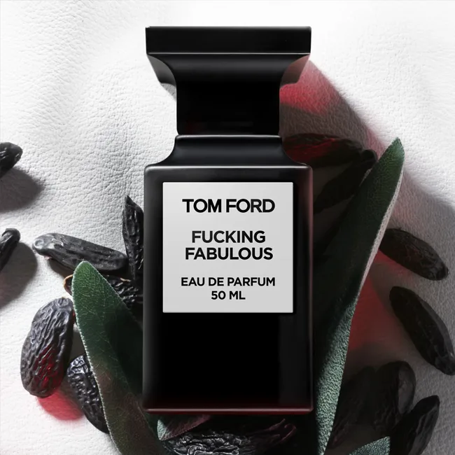 بطری عطر Tom Ford Fucking Fabulous روی پسزمینه چرمی سفید به همراه دانههای تونکا و برگهای مریمگلی.