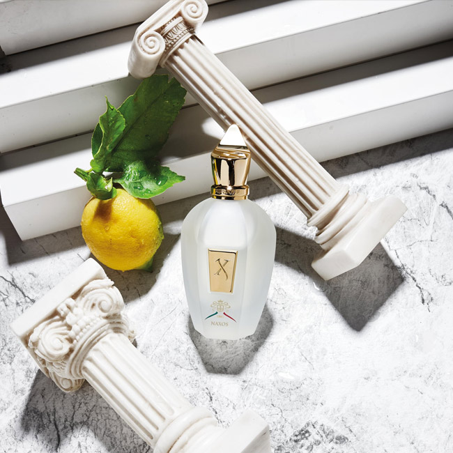 شیشه عطر زرجف ناکسوس میان دو ستون کلاسیک مینیاتوری و یک لیموی تازه با برگ.