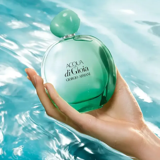 دست زن که بطری عطر سبزرنگ آکوا دی جیویا جورجیو آرمانی را بالای سطح آب آبی درخشان نگه داشته است.