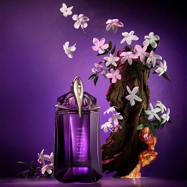 بطری عطر بنفش و کریستالی تیری موگلر آلین در کنار تکه چوب تزئینشده با گلهای سفید و پسزمینه بنفش