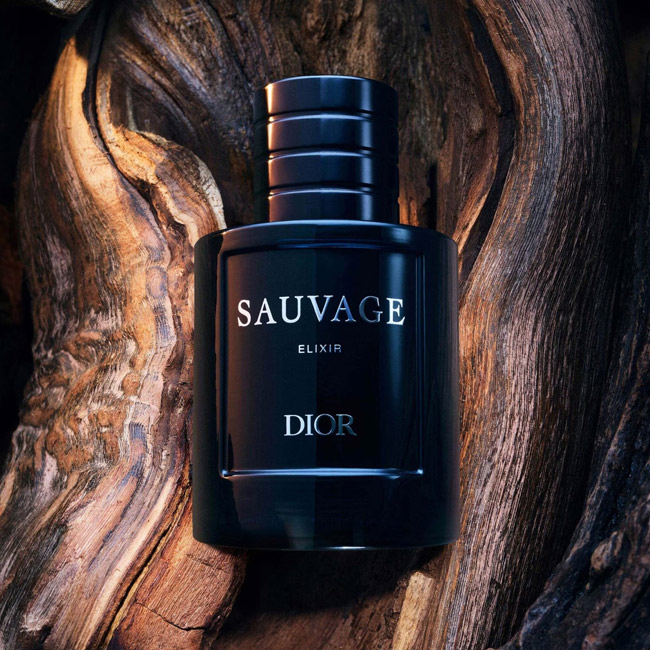 شیشه عطر مردانه دیور ساواج الکسیر با بدنه تیره در میان بافت طبیعی تنه درخت