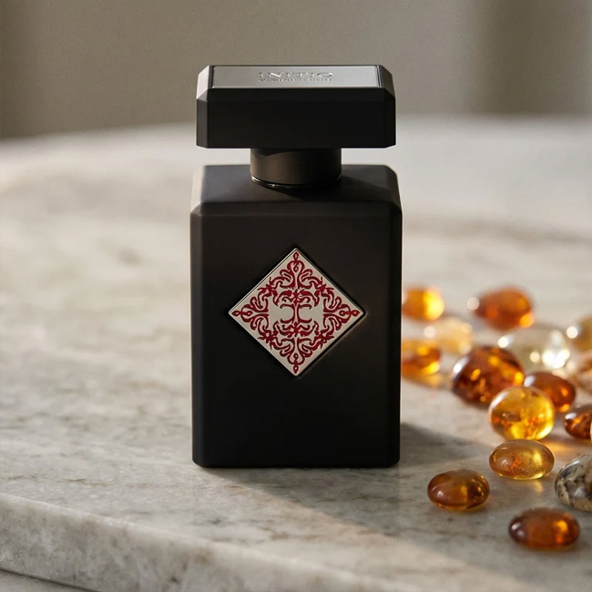 شیشه عطر اینیشیو بلسد باراکا با بدنه مشکی کنار سنگ های کهربایی روی میز سنگی