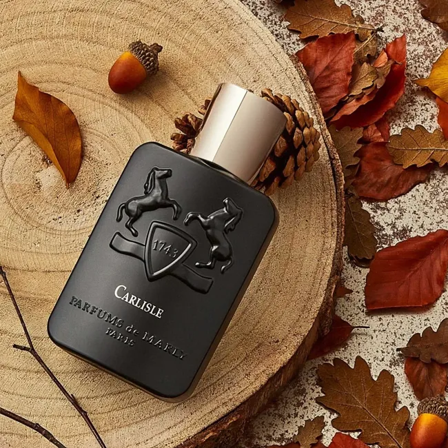 شیشه عطر مشکی پارفومز د مارلی کارلایل روی چوب کنار برگ های پاییزی و بلوط