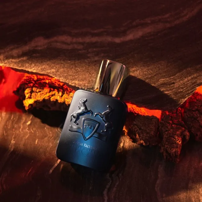 شیشه عطر پارفومز د مارلی لیتون اکسکلوسیف تیره روی تکه چوبهای طبیعی با نورپردازی قرمز و گرم