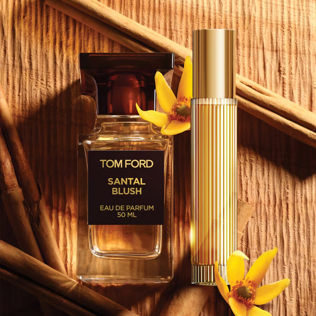 شیشه عطر تام فورد سانتال بلاش کنار اسپری طلایی روی چوب با دارچین و گل زرد