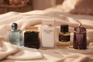 پنج بطری عطر لوکس (آکوآ دی جیویا، دوان، پیور ماسک، دان تس برا، الین) روی پتوهای کشمیری کرم رنگ.